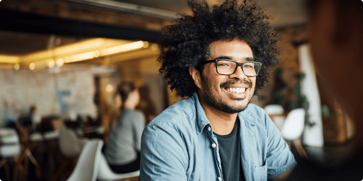 Un homme avec lunettes donne un large sourire dans un café.